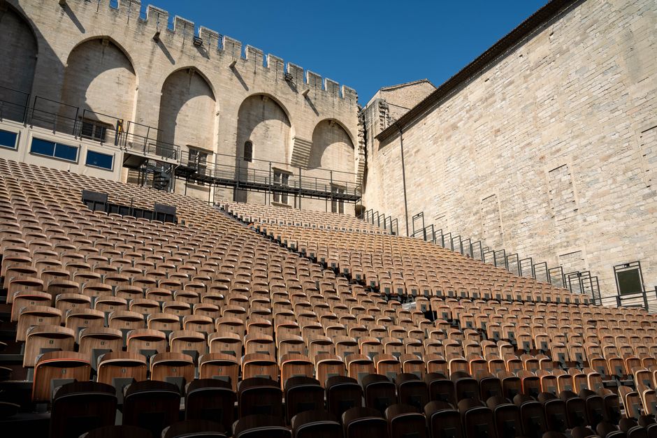 Rows of wooden seats in an empty outdoor theater under blue sky in Avignon, France.
