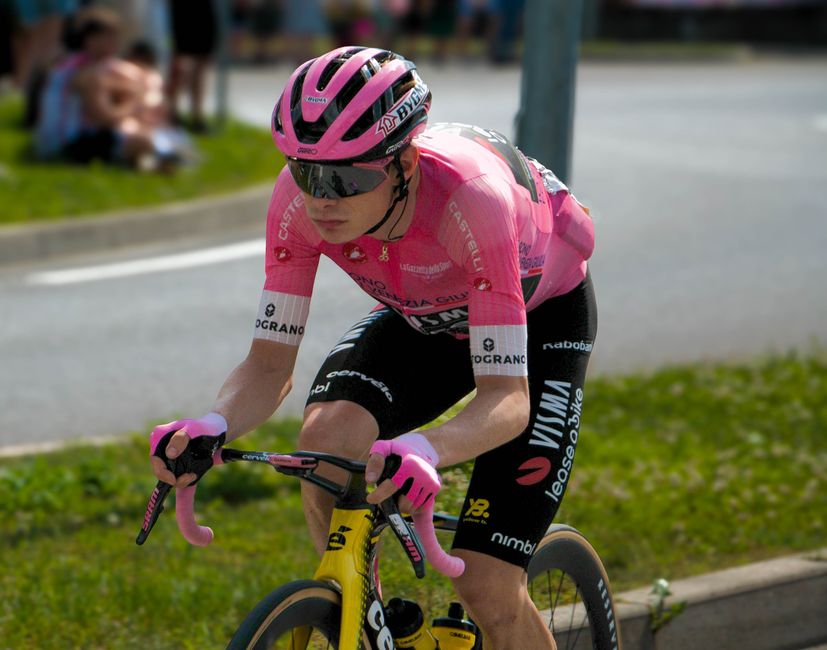 Professional cyclist competing in a race, wearing a distinctive pink jersey and helmet, focused and determined.