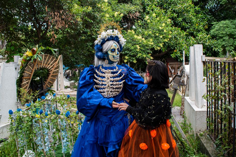 Festive Day of the Dead scene with traditional Catrina costumes in a vibrant cemetery setting.