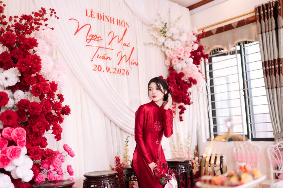Elegant Asian woman in red dress at engagement ceremony with floral decor, Bắc Sơn, Vietnam.