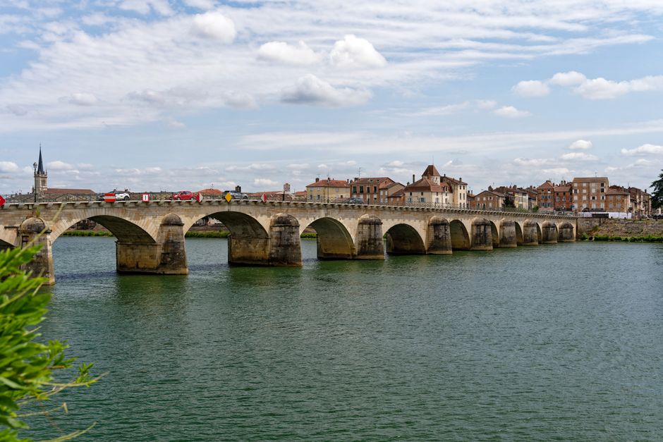 Charming stone bridge crossing the La Saône river in Mâcon, France under a bright sky.