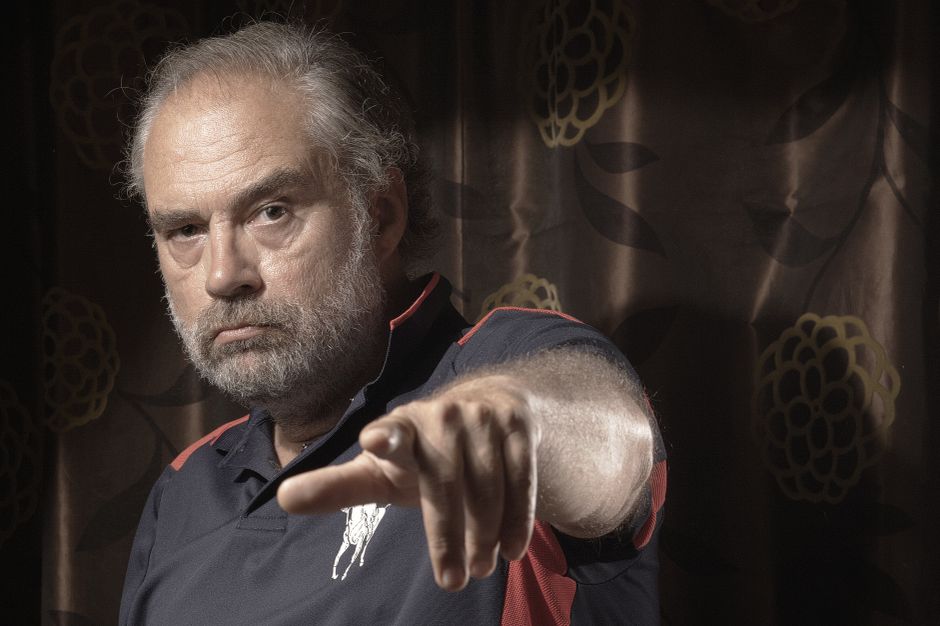 Intense portrait of a middle-aged man with a serious expression and pointing gesture, captured in dramatic lighting.