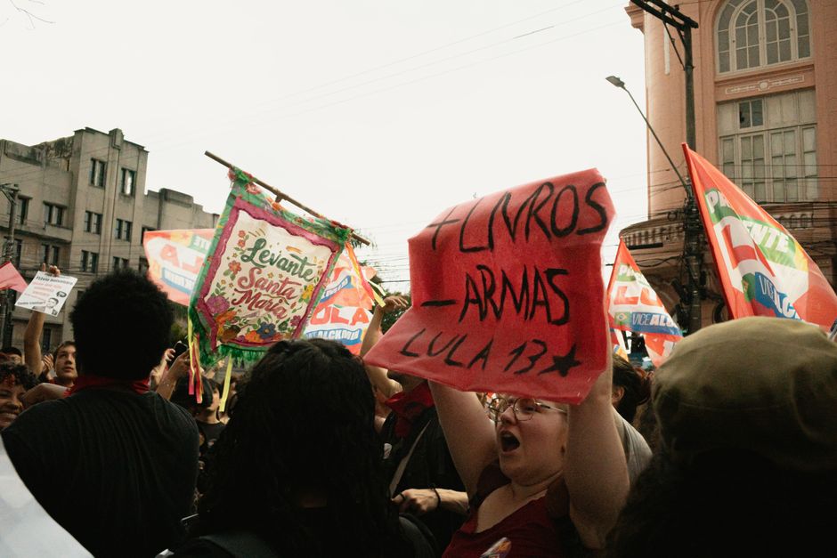 Protesters hold banners and signs during a political rally in an urban street scene.