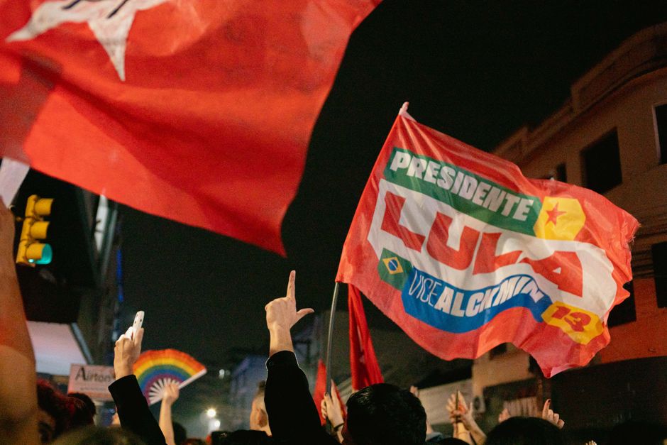 Supporters at a night rally waving flags with political slogans and hand signs.