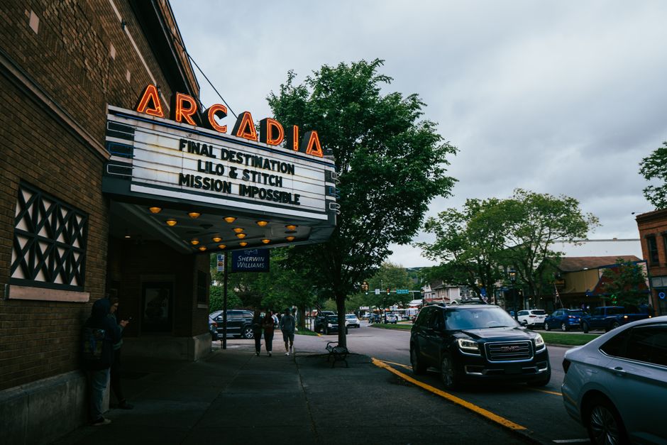 Street view of Arcadia cinema with neon sign displaying movie titles in a lively urban setting.