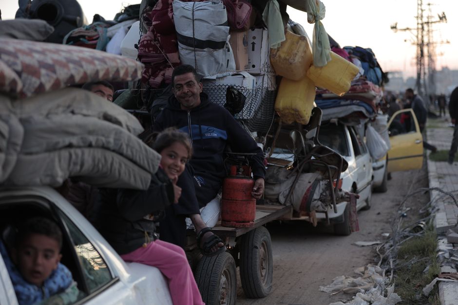 Loaded vehicles with people and belongings on a dirt road at dusk.