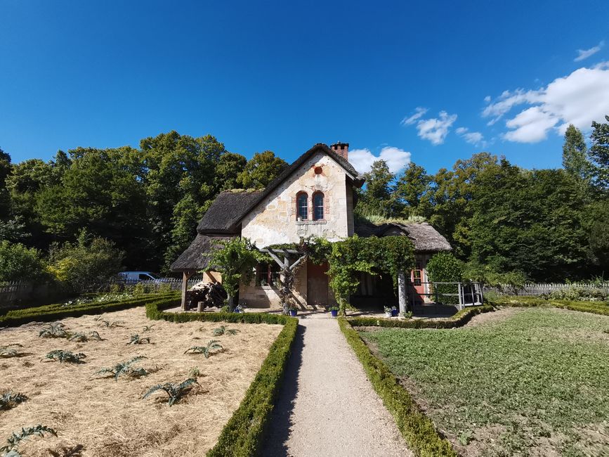 Beautiful rustic cottage surrounded by gardens under a clear blue sky, perfect for a tranquil escape.