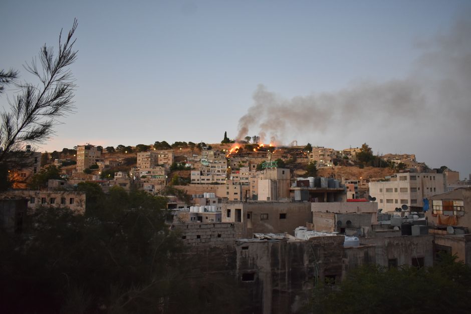 Stunning view of Amman's hilltop buildings with smoke rising, capturing a dramatic sunset cityscape.