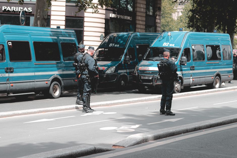Back view of unrecognizable police officers controlling street while standing near police vans in downtown on sunny day