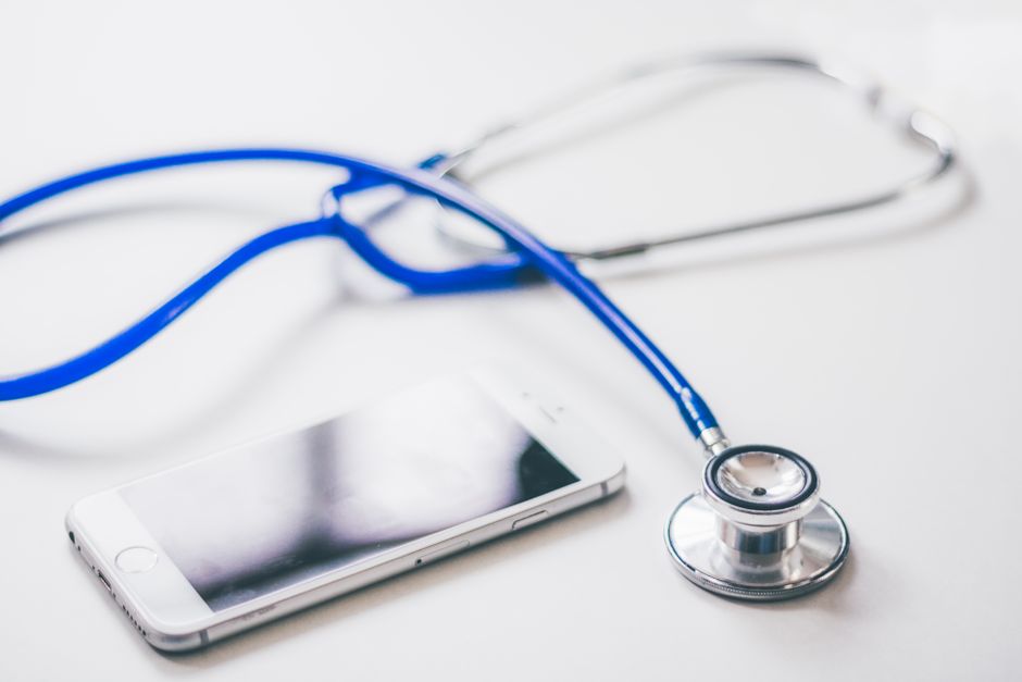 A smartphone and blue stethoscope on a clean white surface, emphasizing modern healthcare.