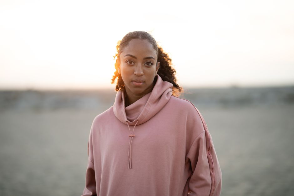 A serene portrait of a woman in a pink hoodie with a sunset backdrop on the beach.