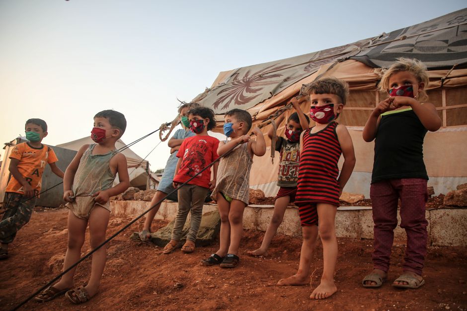 Young children wearing masks in a Syrian refugee camp, highlighting the impact of the pandemic.