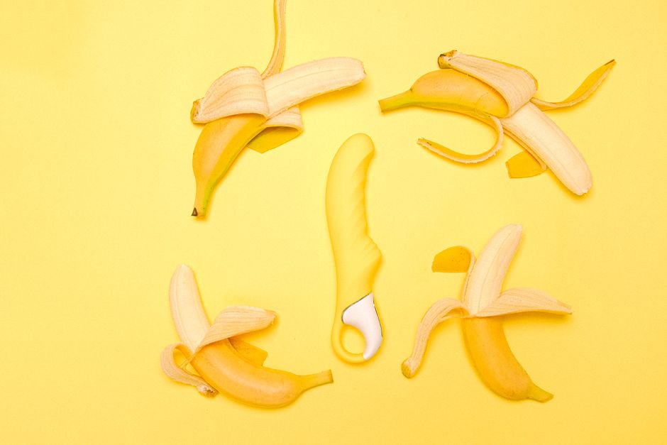 Creative flat lay of a yellow silicone vibrator surrounded by peeled bananas on a yellow background.