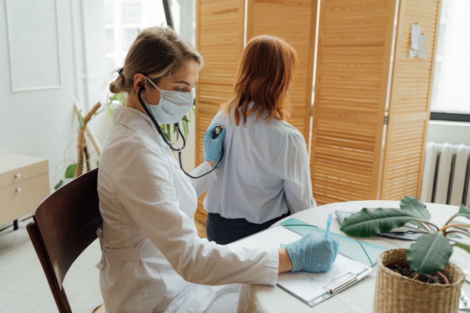 Female doctor examining a patient with a stethoscope in a medical office.