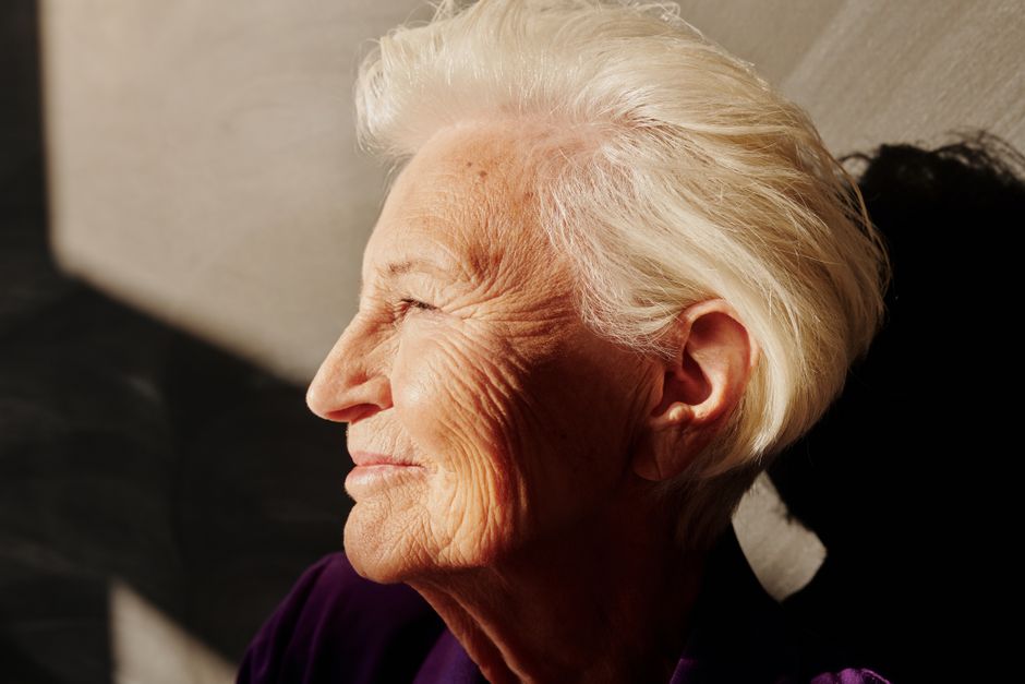 A senior woman with gray hair smiles warmly in the sunlight, showcasing life’s beauty.