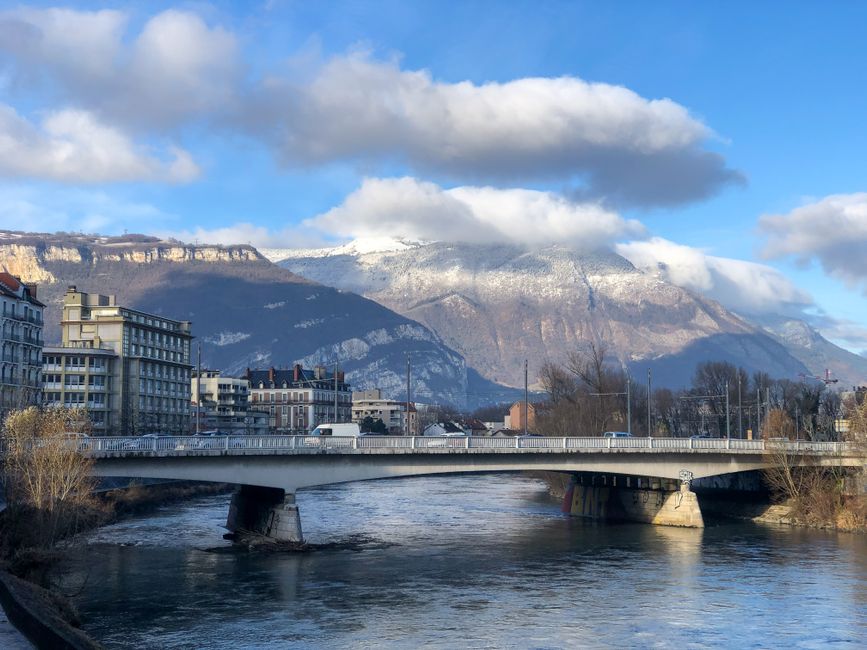 Explore the stunning landscape of Grenoble with mountains, river, and architecture under a blue sky.