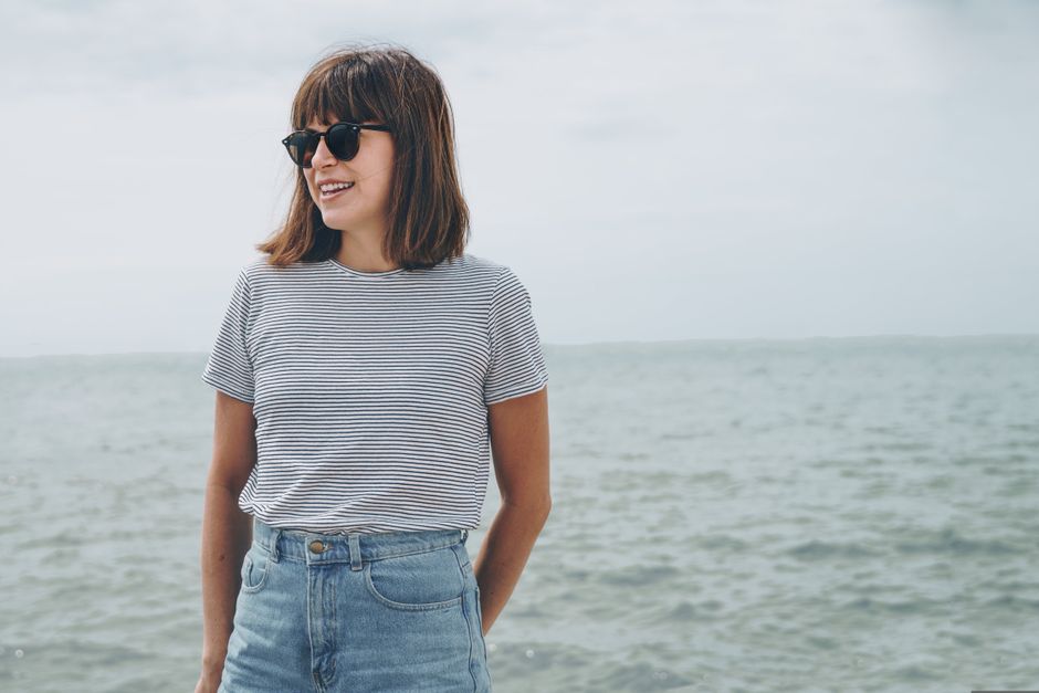 Smiling woman in sunglasses enjoys a sunny day by the ocean, embodying summer leisure and relaxation.