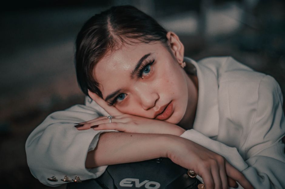 Cool young female in white outfit looking at camera while leaning on motorbike on street against blurred background in countryside