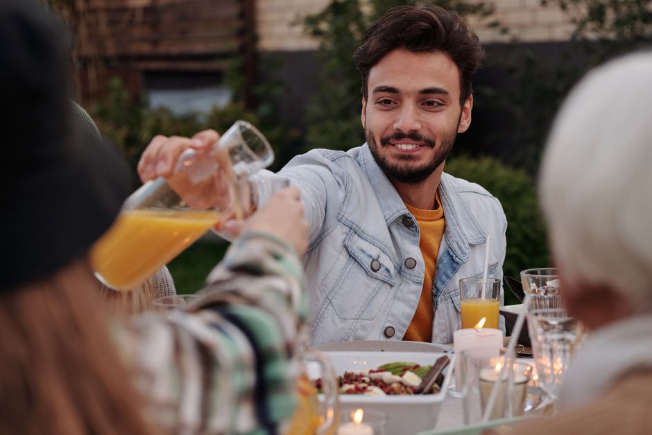 Smiling man pouring juice to girl in glass while sitting table with family in backyard having dinner