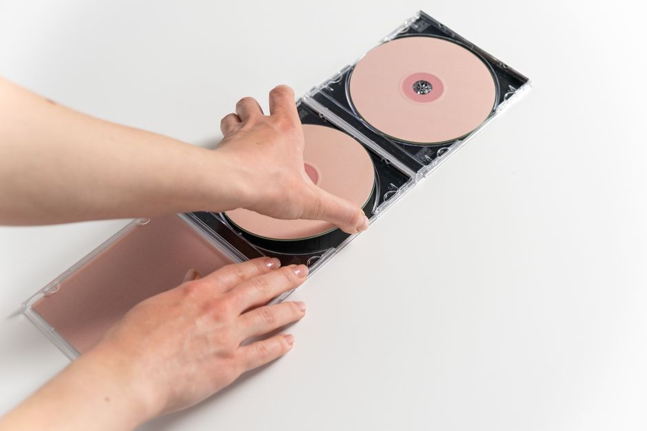 Close-up of hands holding and arranging pink compact discs in a jewel case on a white background.