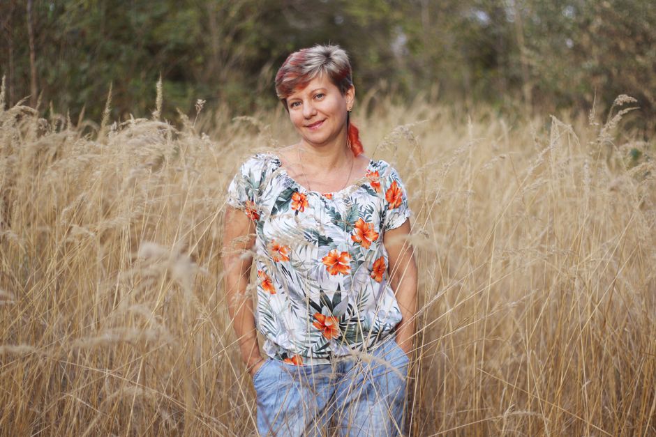 Woman with short hair enjoying a sunny day in a tall grass field, wearing a floral top.