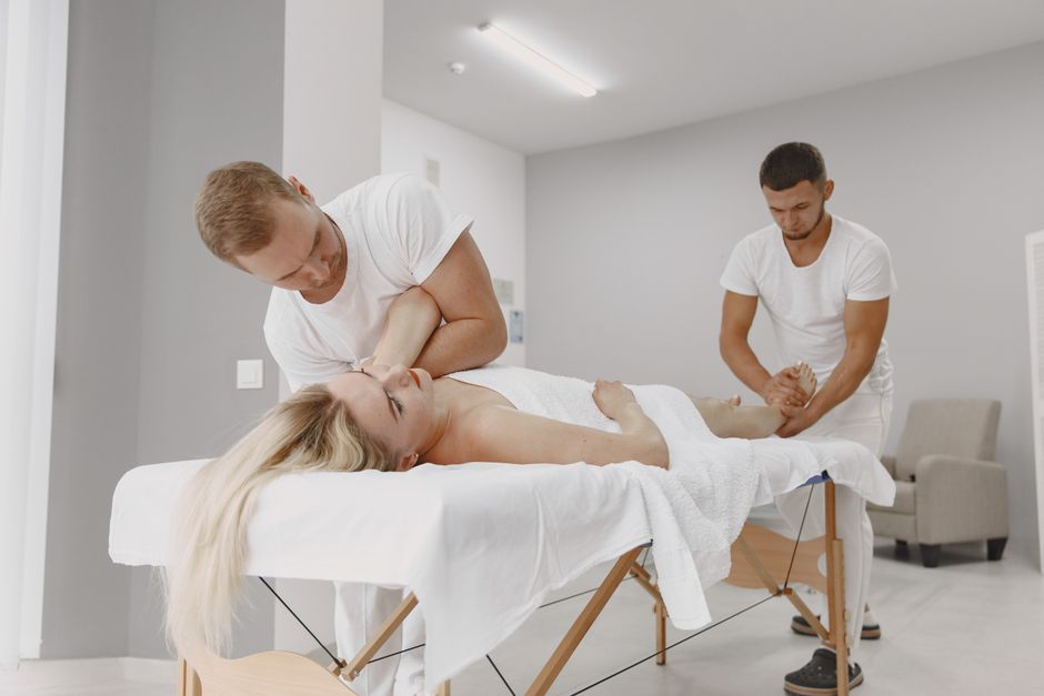 A woman receives a professional massage from two masseurs in a modern spa setting, promoting relaxation and wellness.