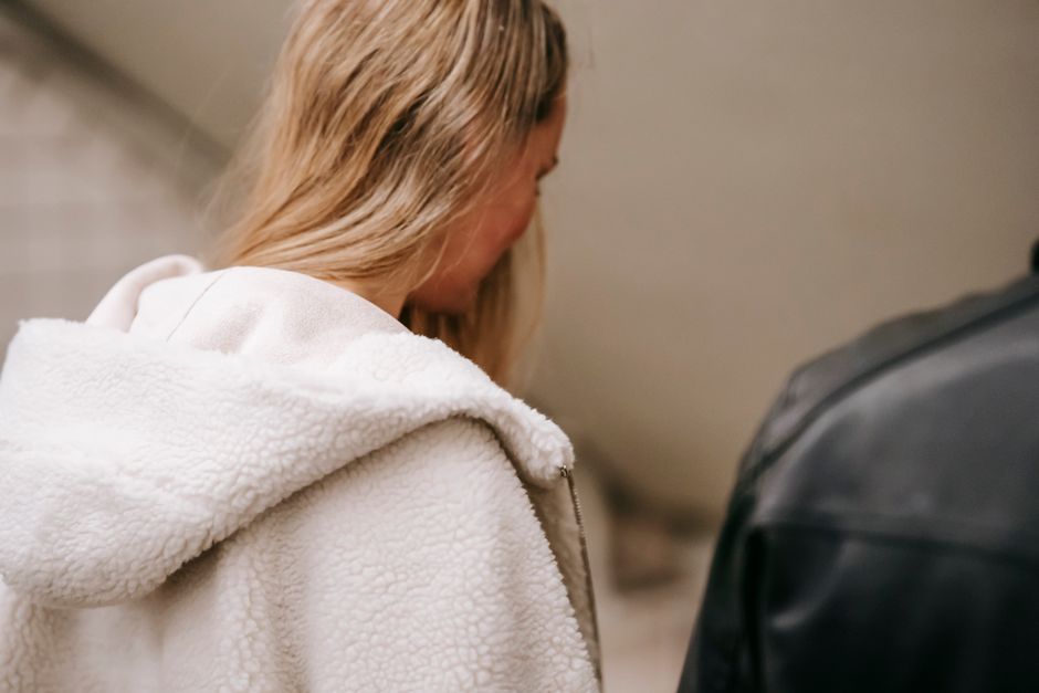 Back view of unrecognizable female with long hair in warm clothes standing in light corridor and looking down