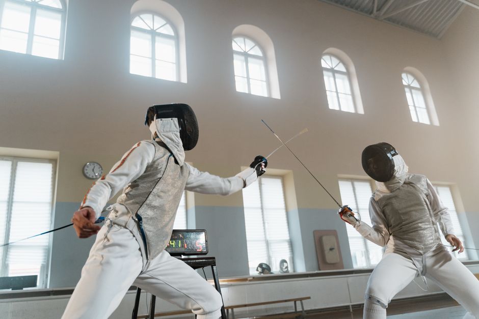 Two athletes engaged in a fencing duel indoors, showcasing skill and precision.