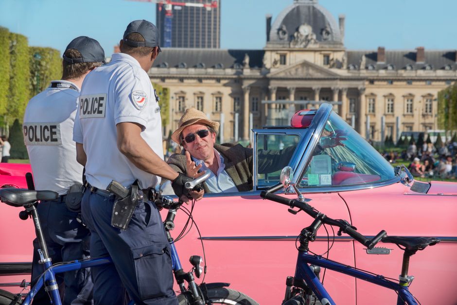 Police officers engage with a classic car driver near the historic École Militaire in Paris on a sunny day.
