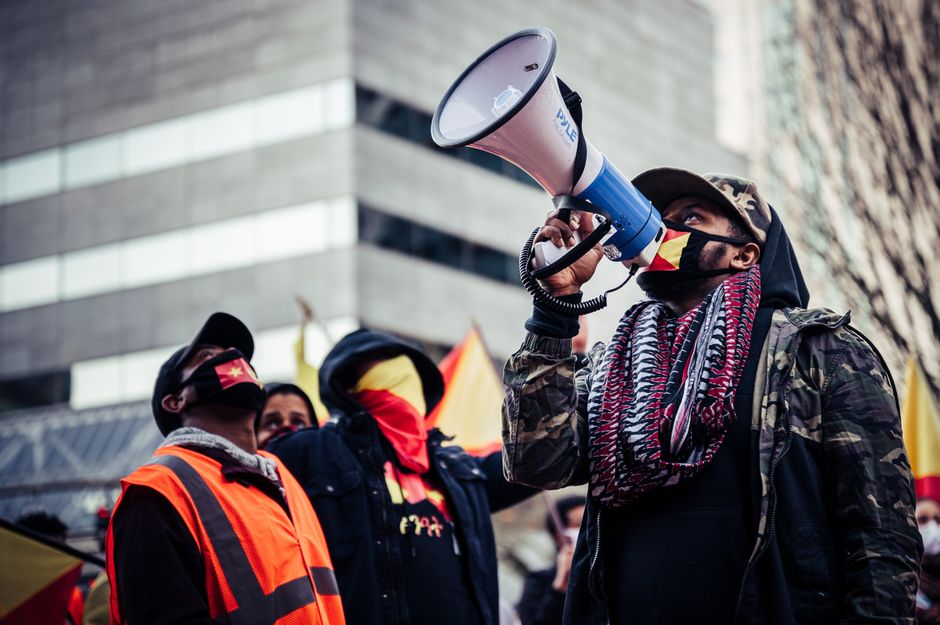 Group of African American people wearing protective masks with loudspeaker standing on street while participating in protest against racism during pandemic