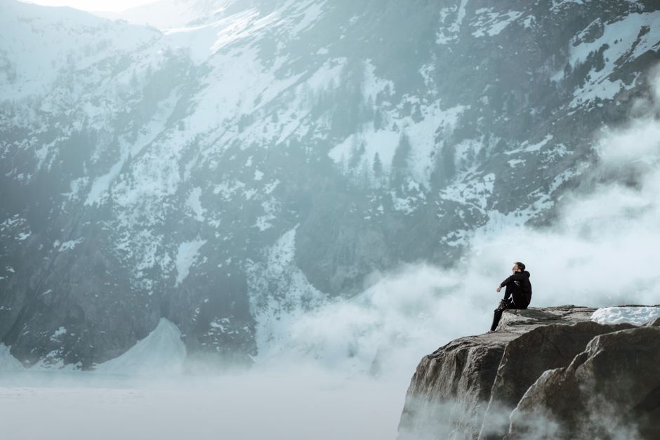 Man sitting on a cliff edge overlooking snowy mountains and mist in France.