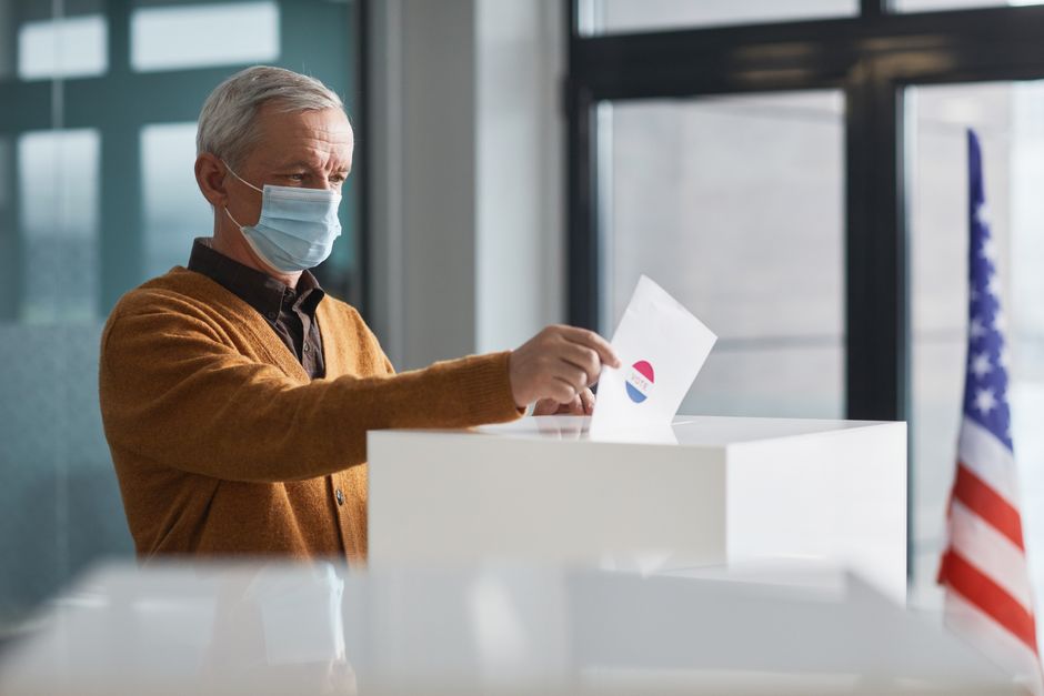 An elderly man wearing a face mask votes in-person, highlighting safety during the pandemic.