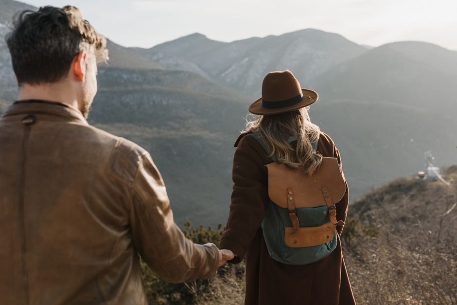 A couple holds hands while enjoying a scenic mountain hike, symbolizing travel and love.
