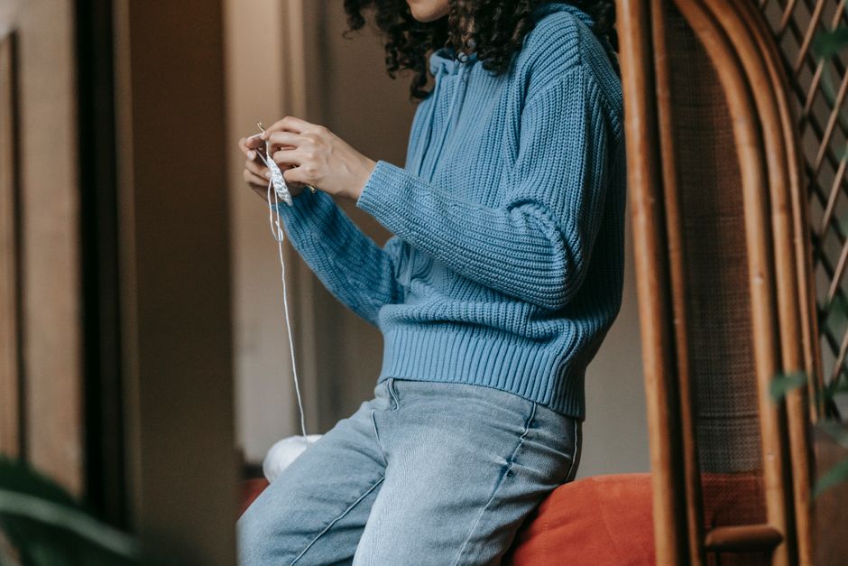 Close-up of a woman knitting in a blue sweater, showcasing handmade craftsmanship.