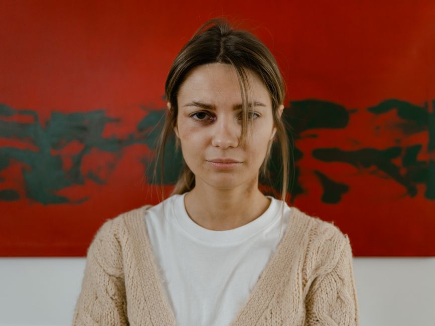 A woman stands pensively with a red abstract art background, expressing contemplation.