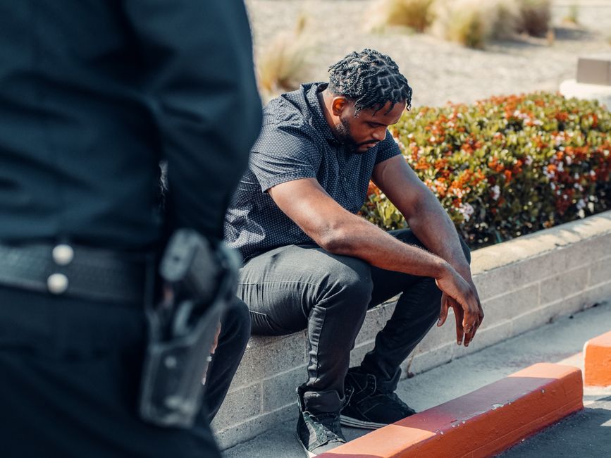 A police officer watches over a seated suspect outdoors, conveying law enforcement dynamics.