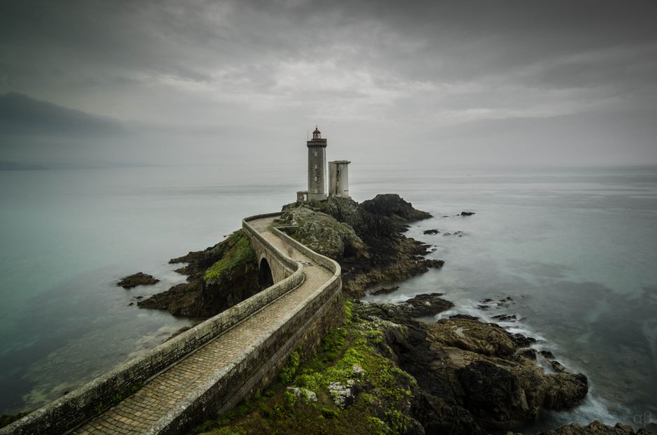 A scenic view of Le Phare du Petit Minou lighthouse on a cloudy day, situated on a rocky coast in Bretagne, France.