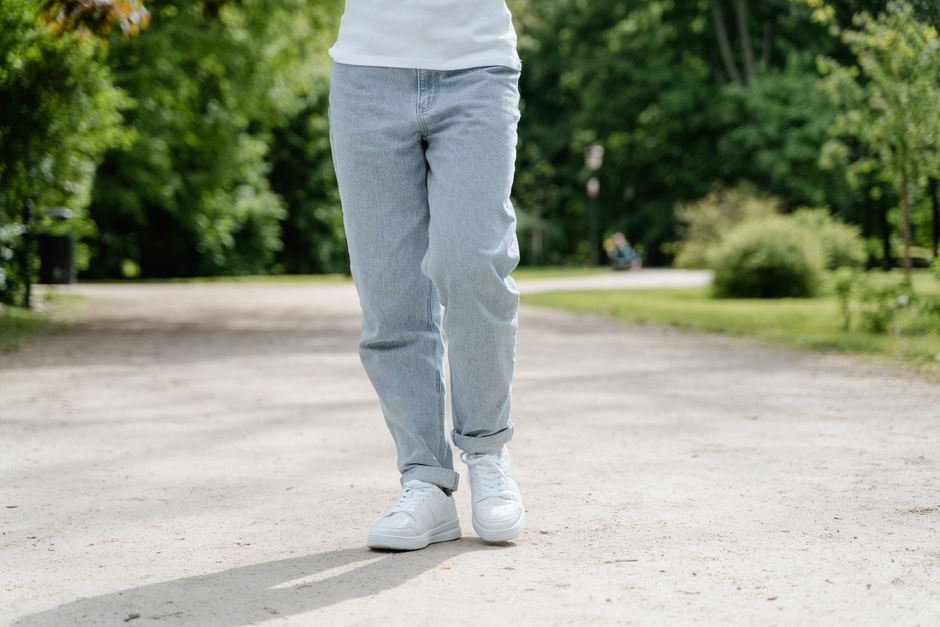 A close-up view of a person walking on a park pathway wearing blue jeans and white sneakers.