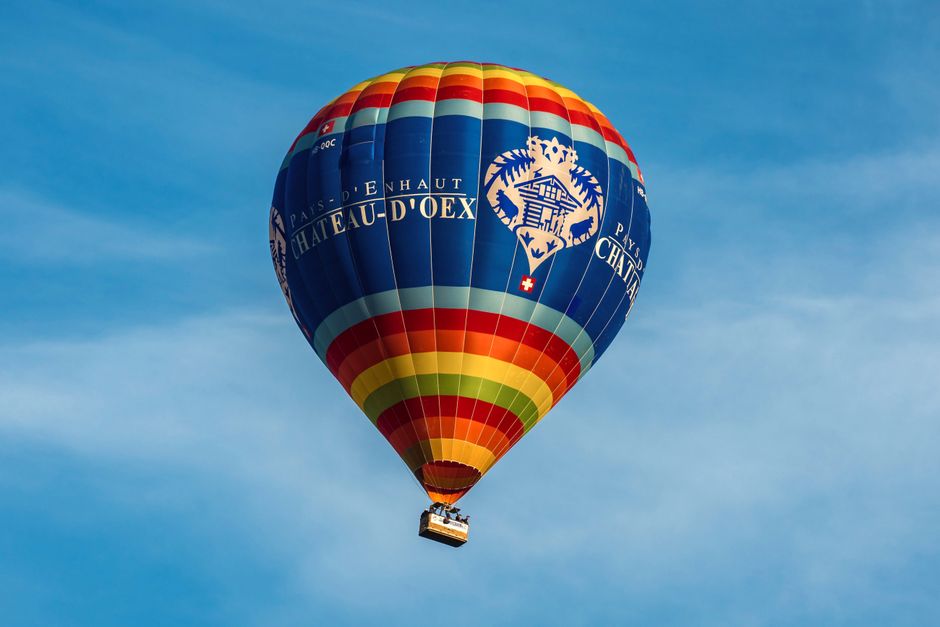 Vibrant hot air balloon floats in the blue sky above Château-d'Oex, Switzerland.