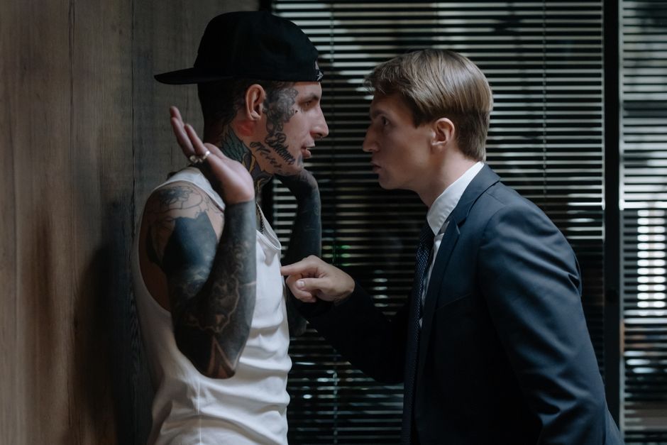 A tense indoor scene depicting an intense interrogation confrontation between two men.