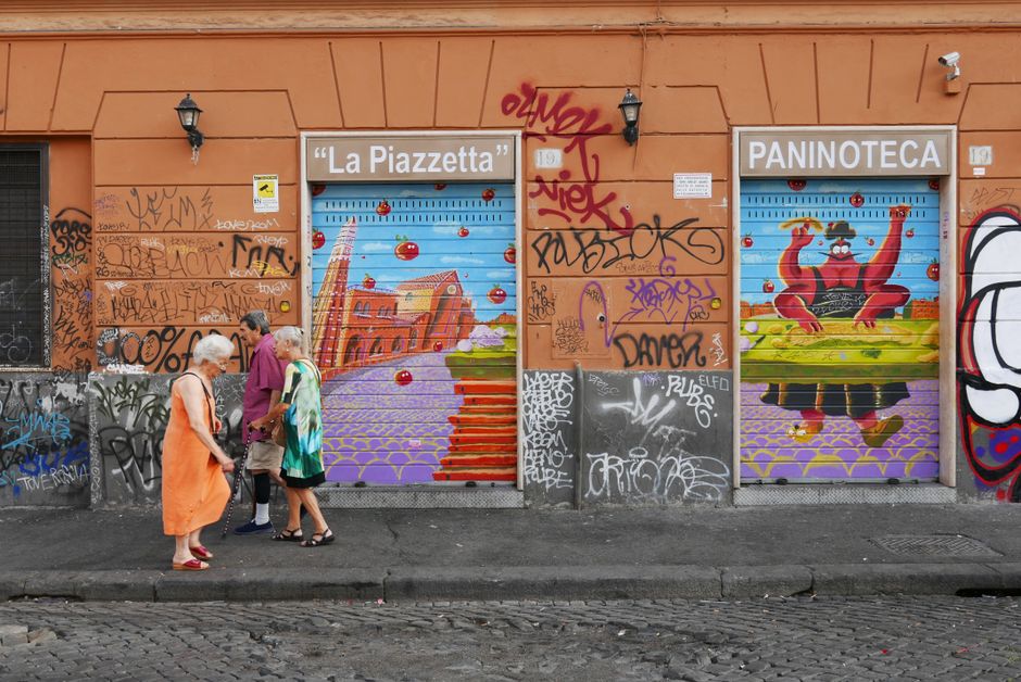 Vibrant street art on a graffiti-covered wall in Rome, Italy with people passing by.