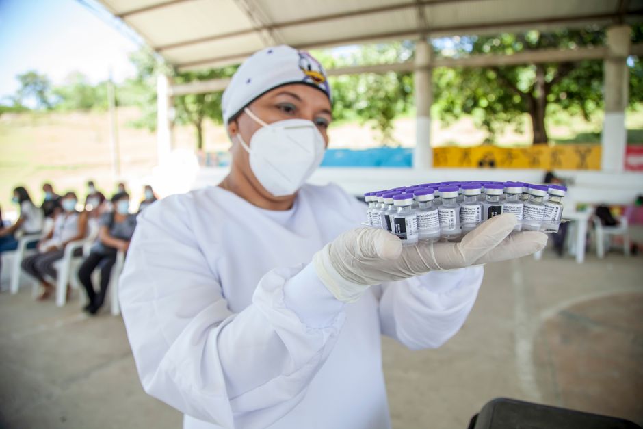 Health worker in Colombia holding vaccine vials at an outdoor vaccination site.