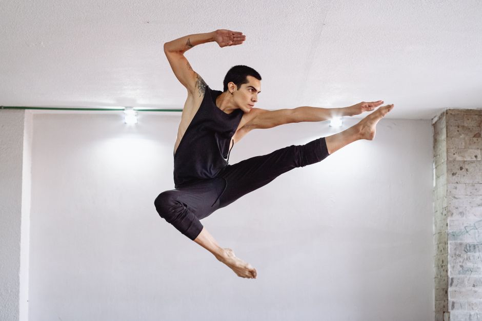 Male dancer performing an impressive jump in a dance studio, showcasing skill and flexibility.