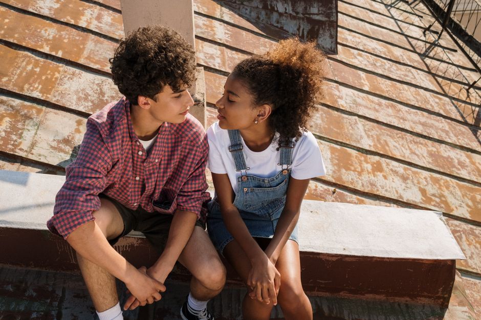 A young couple sitting closely on a sunlit rooftop, sharing a moment together.