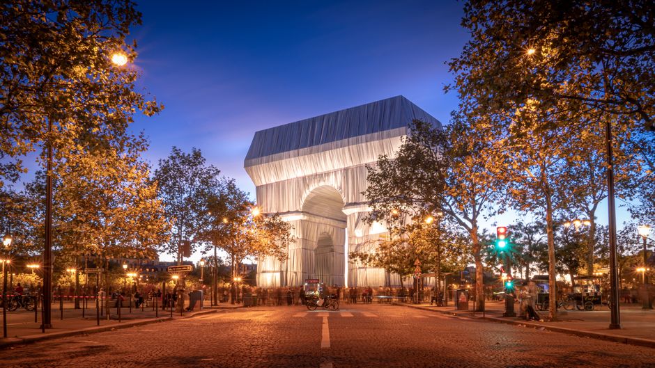 The iconic Arc de Triomphe wrapped in fabric, illuminated at night in Paris.