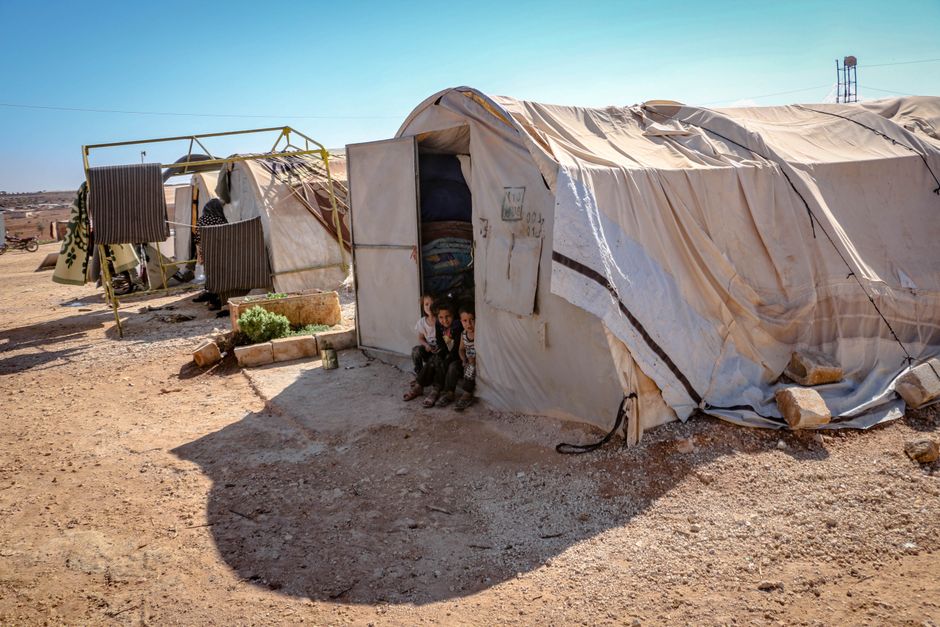 Young children standing near tents in a refugee camp in Idlib, Syria. Focus on poverty and displacement.